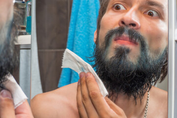 A man with a beard got dirty with blue paint and is now wiping his beard with a napkin