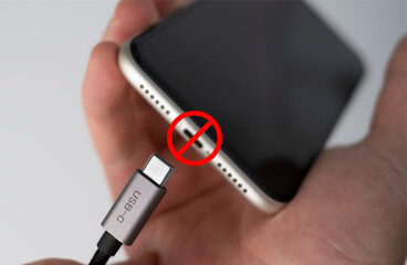 EU, electronic waste for proposes mandatory USB-C on all devices. Hand trying to plug type-c cable into smartphone.