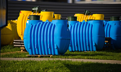 Plastikowe zbiorniki do przydomowych oczyszczalni ścieków . Żółty , niebieski . Beczka metalowy płot . Plastic tanks for home sewage treatment plants. Yellow, blue. Barrel, metal fence.  - obrazy, fototapety, plakaty