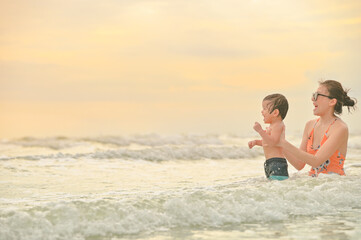 Happy family resting at beach in summer, Mother and baby boy feet at the sea foam at the sunlight water is moving