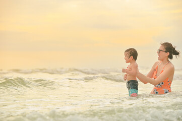 Happy family resting at beach in summer, Mother and baby boy feet at the sea foam at the sunlight water is moving