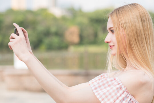 Happy and beautiful caucasian blonde girl holding a smartphone in her hands and taking picture