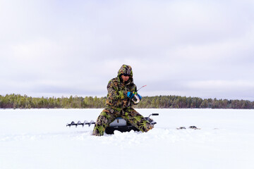 A fisherman in special clothes catches fish in winter on the lake. The concept of survival in the wild in winter