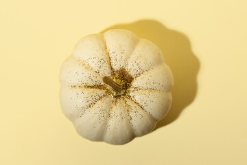 White pumpkin on the yellow background with golden glitter,top view.