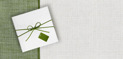 gift card, white gift box and green string ribbon bow and label, isolated on green and gray fabric...