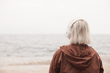 Back view of a blonde woman listening to music and looking at the sea
