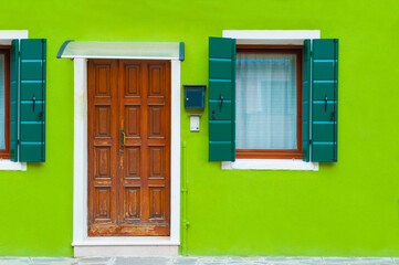 Green facade of the house with wooden door and windows. Colorful architecture in Burano island, Venice, Italy.