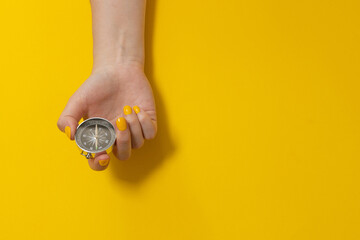 Tourist hand holding a compass on a yellow background with copy space. Journey, adventure lifestyle. Road to home. Trip.