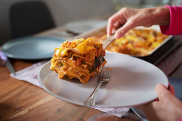 Female hand placing delicious vegan lasagna on a plate - obrazy, fototapety, plakaty