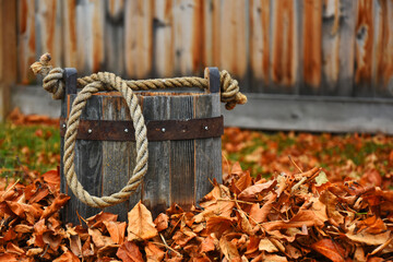 An image of an old vintage wooden pail with a rope handle in a pile of brightly colored autumn leaves. 