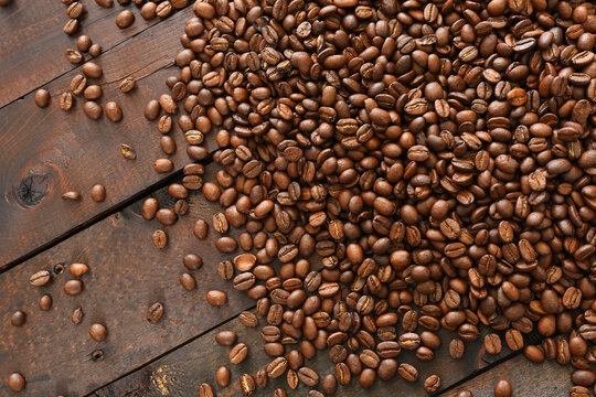 A close up image of dark roasted coffee beans spilled on a dark wooden table top. 
