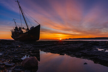 Stranded old fishing schooner at beautiful dawn. The old ship is covered in rust. Rocky coastline of the Barents Sea, Rybachy Peninsula. 
