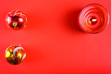 Two Christmas balls and a candle on a red background with a spear space.