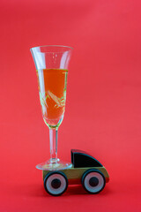 Fougere with champagne rides on a toy car on a red background.