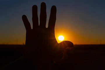 Silhouette of a hand with the sunset sun between the fingers