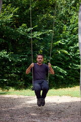 A young cheerful Caucasian male sitting on a swing in a park at daytime