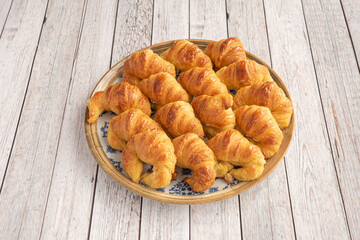 Gold rimmed blue plate filled with mini butter croissants on light wooden table