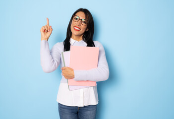 Smiling woman holding books. isolated portrait of school teacher pointing finger up isolated over blue background.