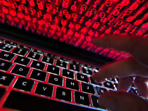 Hacker coding a computer virus infecting a laptop