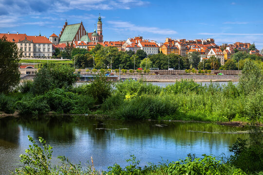 Poland, Masovian Voivodeship, Warsaw, Overgrown riverbank of Vistula river with skyline of Warsaw Old Town in background