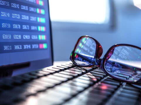 Stock market data reflecting in eyeglasses lying on laptop keyboard