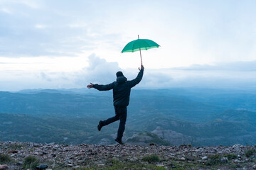 Man jumping for joy on a mountain, holding a green umbrella