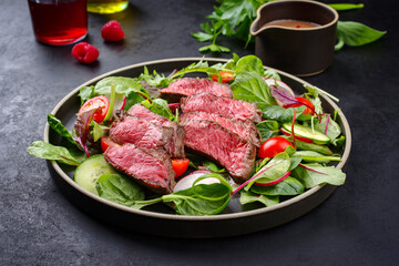Modern style traditional fried dry aged bison beef rump steak slices with vegetable, lettuce and mustard dressing served as close-up on a Nordic design plate