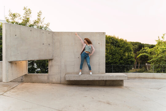Young redheaded woman with raised arm on concrete bench