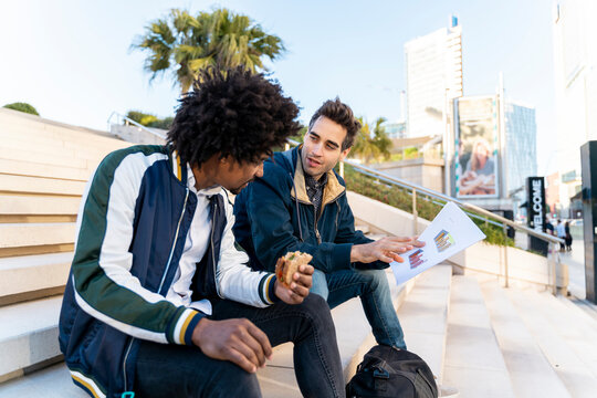 Two casual businessmen sitting on stairs working on paper