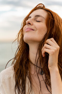 Portrait of happy redheaded young woman with nose piercing in front of the sea by sunset