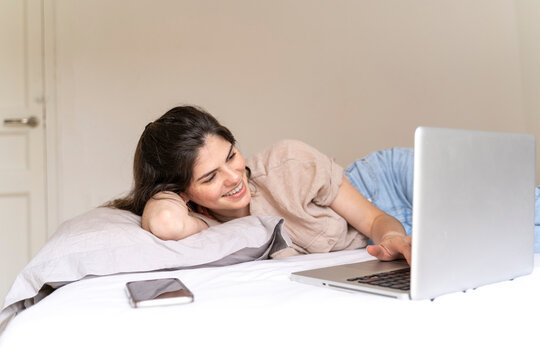 Happy young woman lying on bed using laptop