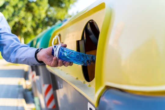 Close-up of man putting plastic bottle into recycling bin
