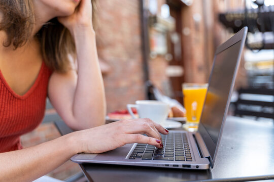 Young blogger sitting at street cafe working on laptop, close-up