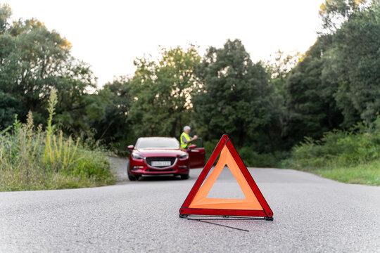 Warning triangle in front of a senior man's broken car on a country road