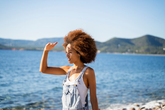 Young woman on the beach, shielding her eyes with her hand