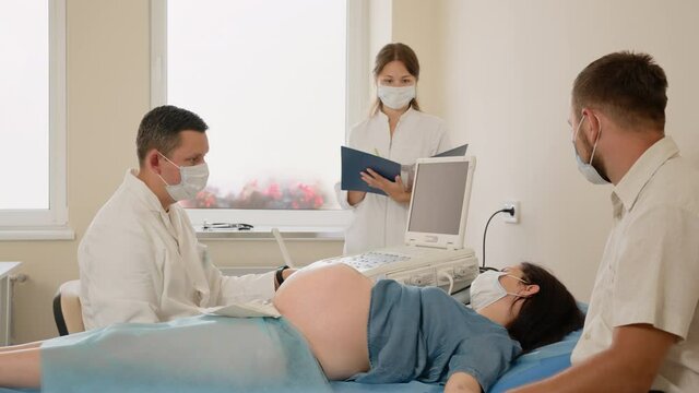 Pregnant woman with caring husband visiting medical clinic for regular diagnostic. Competent gynecologist doing ultrasound screening for patient. Concept of pregnancy, support and health care.