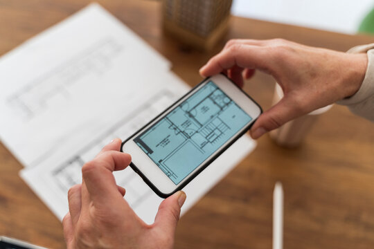 Close-up of woman in architectural office taking cell phone picture of construction plan