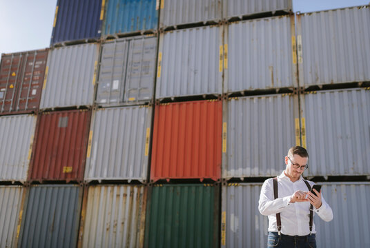 Manager in front of cargo containers on industrial site using cell phone