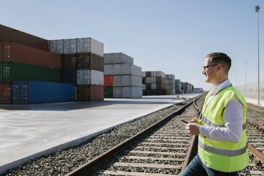 Man on railway tracks in front of cargo containers holding cell phone