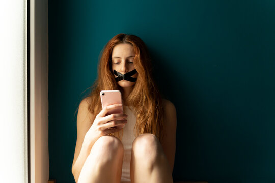 Young woman with taped mouth using cell phone