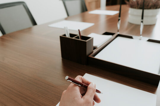 Hand holding ballpen at conference table in office
