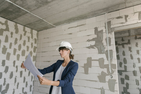 Female architect checking architectural plan on construction site