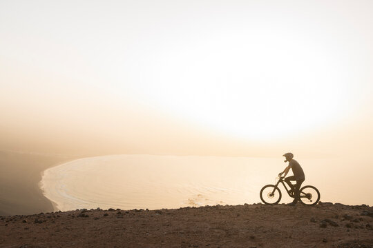 Spain, Lanzarote, mountainbiker on a trip at the coast at sunset
