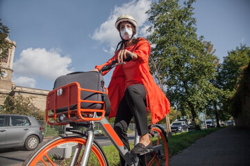 Young woman with helmet and face mask, riding bicycle in the city
