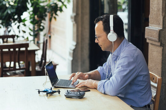 Businessman with headphones, laptop and drone in a coffee shop