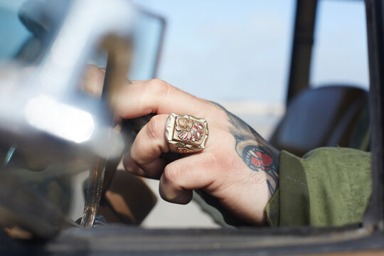 Man's hand with ring and tattoo at car steering wheel