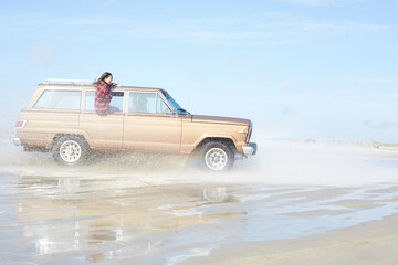 Germany, St Peter-Ording, girl leaning out of window of off-road vehicle driving through water on...