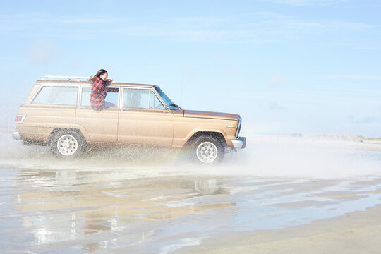Germany, St Peter-Ording, girl leaning out of window of off-road vehicle driving through water on the beach