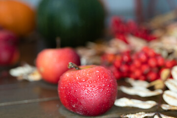 Autumn still life, on a wooden table. in the rain. Red apples, red rowan pumpkins.