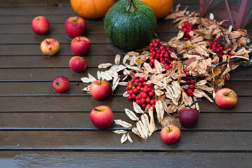 Autumn still life, on a wooden table. in the rain. Red apples, red rowan pumpkins.